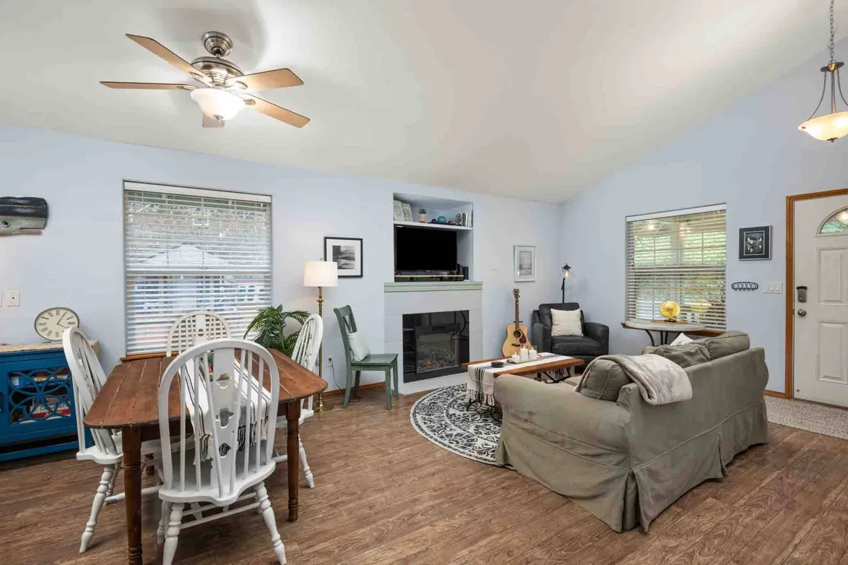 A spacious open-concept living and dining area featuring a comfortable sofa, a cozy electric fireplace, a dining table, and a television. The room is filled with natural light, creating an inviting, relaxed atmosphere ideal for group gatherings and family time.