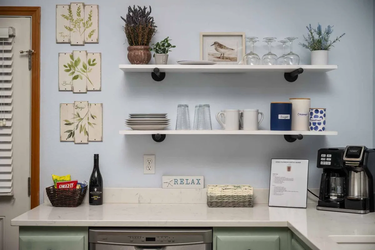 A welcoming view of the kitchen shelves filled with dishes, glasses, and decorative plants. A bottle of wine and a coffee maker add an inviting, lived-in touch, while a 'relax' sign creates a sense of comfort and reassurance.