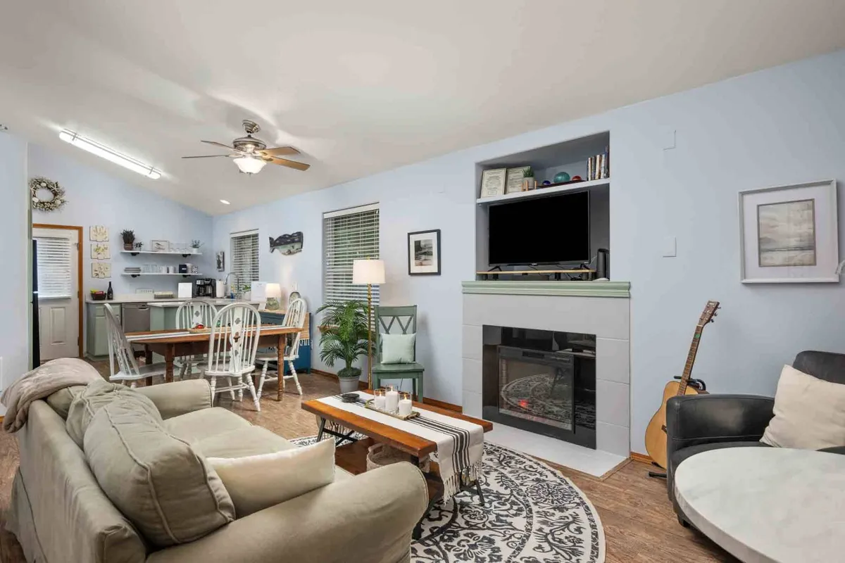 A warm, inviting living room with a plush sofa facing an electric fireplace, dining table, guitar for music, and decorative accents. The setup glows with comfort and togetherness, making it perfect for relaxing, entertaining, or sharing memorable moments.