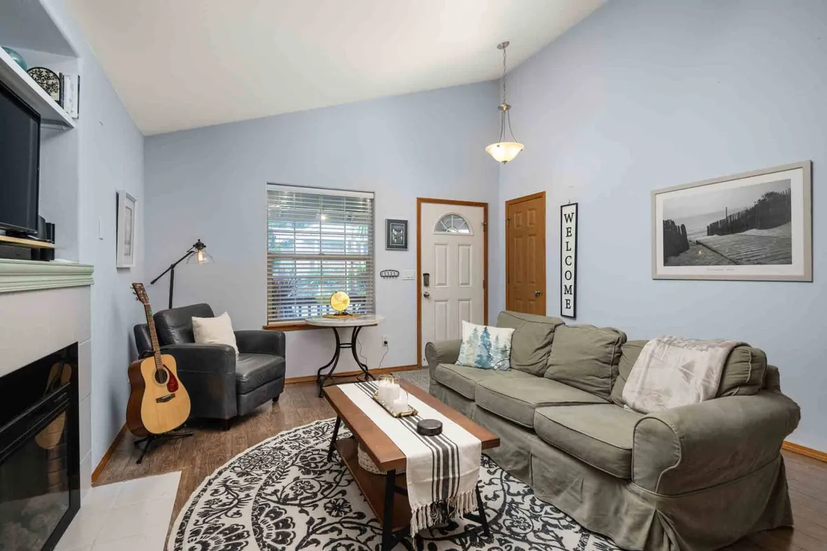 A welcoming living area with a plush sofa, coffee table, guitar, lamp, and a visible 'welcome' sign. The layout is inviting, suggesting a space for movie nights, playing music, or unwinding with loved ones.