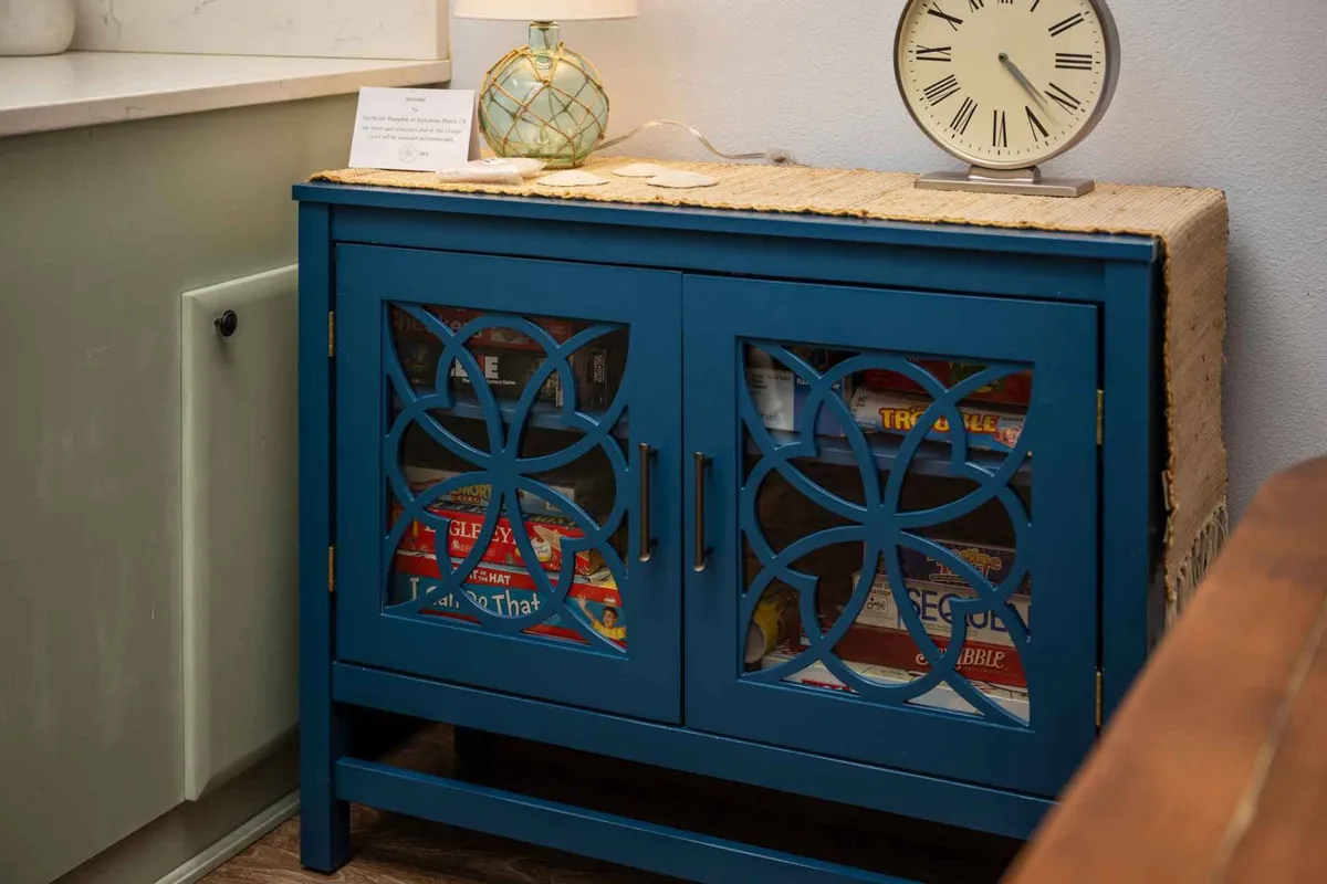 A welcoming family room scene featuring a blue cabinet, decorative lamp, and wall clock, with a textured table runner. The space is set for casual conversations, game nights, and quiet moments, radiating warmth and hospitality.