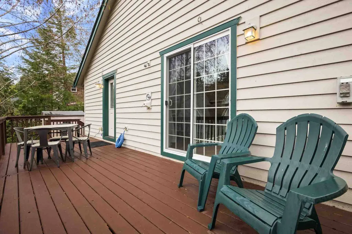 A spacious patio area with deck chairs and a dining table set near a sliding glass door, offering a comfortable spot for outdoor dining or morning coffee. Trees and foliage around the deck provide privacy and a natural atmosphere.
