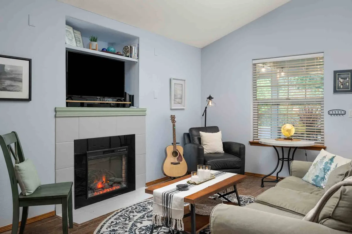 A cozy living space featuring a fireplace, a guitar, and a coffee table, suggesting relaxation, music, and leisure time. The lighting and decor foster a sense of warmth and comfort.