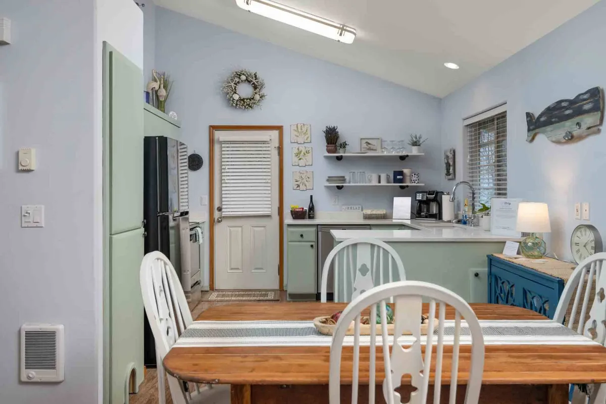 A cozy interior shot highlighting a wooden dining table adjacent to the kitchen counter, with decorative wall art and visible appliances creating an inviting space for meals and gatherings.