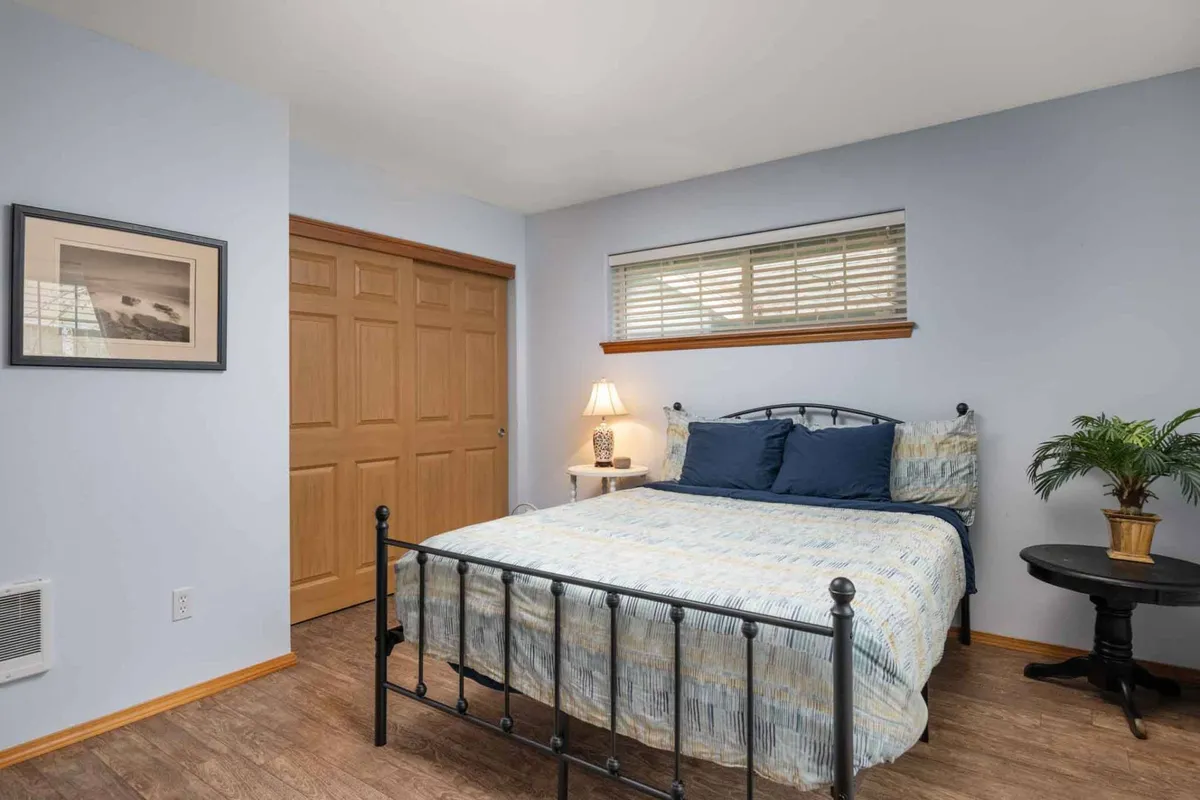 This image features a bed with soft blue bedding, a nightstand with a lamp, and a potted plant by the window. The room is bathed in natural morning light, creating a cozy and tranquil atmosphere ideal for restful sleep.