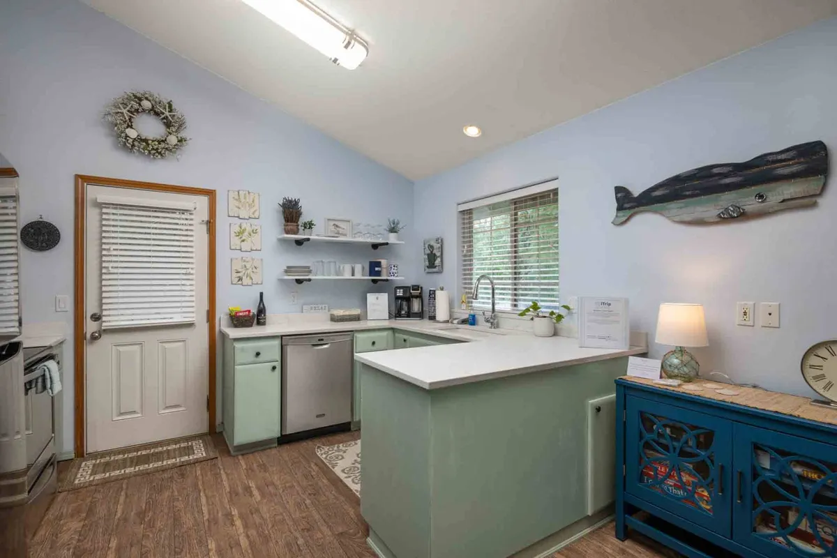 This image displays a warm and welcoming kitchen corner, featuring a blue cabinet, kitchen counter, whale-themed wall art, and a sunlit window. The arrangement suggests relaxed meal prep and social interaction.