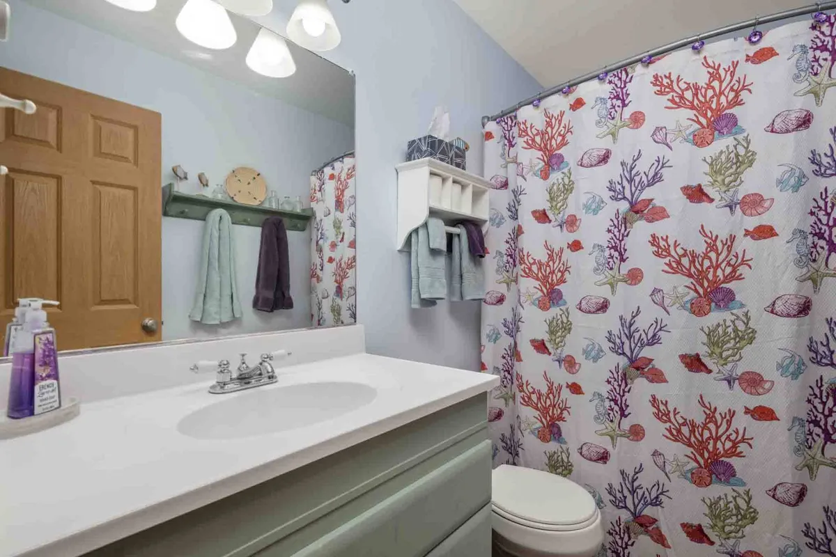 A cheerful bathroom scene with a colorful shower curtain, a modern vanity and sink, and a large mirror. The space feels fresh, clean, and inviting, perfect for morning routines or relaxing baths.