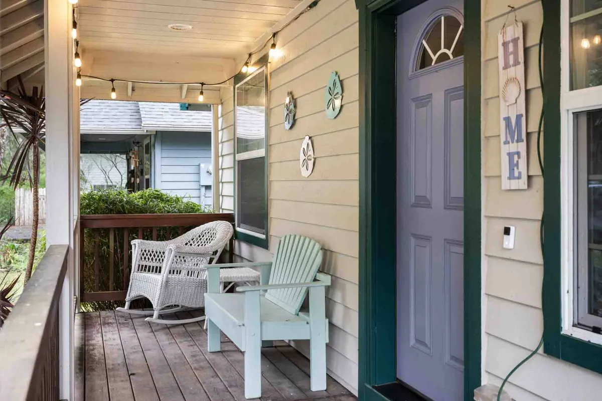 The cozy, inviting front porch of the bungalow showcasing a blue front door, white wicker chair, light string decorations, and decorative wall art. The ambiance is warm and welcoming, ideal for relaxing after a day of downtown or beach adventures.